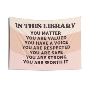 May include: A tapestry with a peach and cream background featuring the text "In this library, you matter, you are valued, you have a voice, you are respected, you are safe, you are strong, you are worth it."