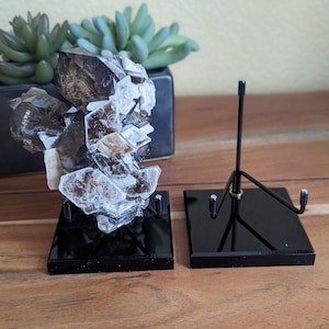 May include: A large, clear, and brown crystal cluster on a black display stand. The crystal is on a black stand with a metal rod.