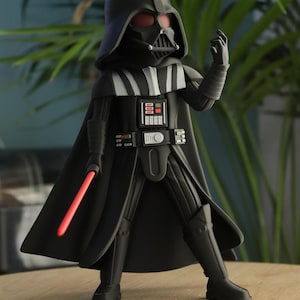 Puede incluir: Una figura negra de Darth Vader con un sable de luz rojo. La figura lleva un casco, capa y armadura negros. La figura está de pie sobre una superficie de madera con una planta verde en el fondo.