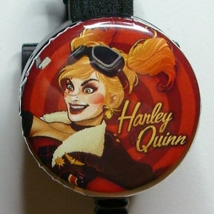 May include: A red and white retractable badge holder with a Harley Quinn image. The image shows Harley Quinn wearing a black leather jacket and goggles. The text "Harley Quinn" is written in gold letters on the badge holder.