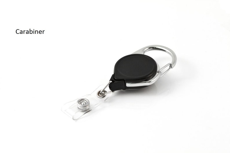 Puede incluir: Un mosquet&oacute;n negro y plateado con un cable retr&aacute;ctil y un porta-credenciales de pl&aacute;stico transparente. El mosquet&oacute;n tiene un dise&ntilde;o circular y el texto "Carabiner" es visible.