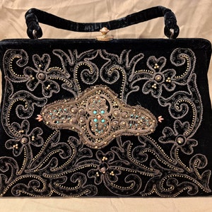 May include: A black velvet handbag with a gold and brown embroidered floral design. The handbag has a top clasp and a single handle.