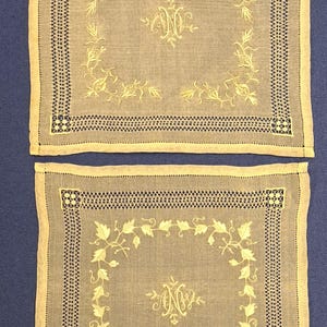 Puede incluir: Dos pañuelos de lino beige con diseños florales bordados en oro y las iniciales "NC".