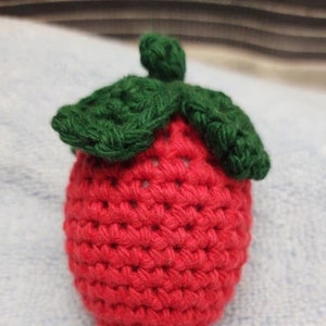 May include: A crocheted strawberry with a green crocheted leaf on top. The strawberry is red and the leaf is green.