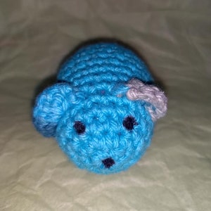 May include: A crocheted blue mouse toy with black eyes and a gray ear.