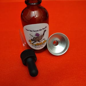 May include: A brown glass bottle with a white label that reads "Treat Your Ferrets Like Royalty." A black dropper and a silver funnel are next to the bottle. The label features a cartoon ferret riding a bird. The background is red.