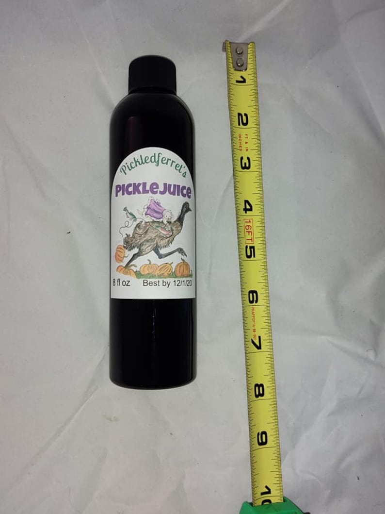 Puede incluir: Una botella de vidrio negro con una etiqueta blanca que dice "Pickledferret's PICKLE JUICE" y presenta una ilustraci&oacute;n de dibujos animados de un em&uacute; con un vestido morado y montando una calabaza. La etiqueta tambi&eacute;n dice "8 fl oz Best by 12/1/20".