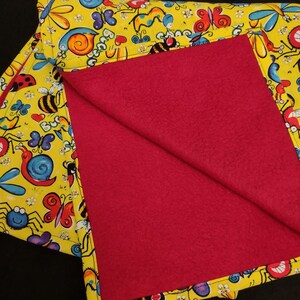 May include: A yellow blanket with a red fleece lining. The blanket features a colorful pattern of bugs, butterflies, and flowers.