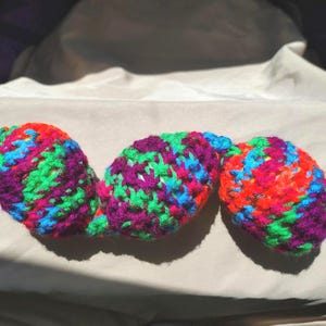 May include: A colorful, handmade crochet item with three connected, oval-shaped pieces. The yarn is a mix of vibrant colors including red, orange, green, blue, and purple. The item is likely a decorative or functional piece.