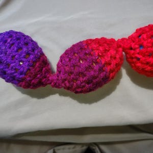May include: A handmade crochet garland featuring three connected, bulbous shapes. The first is a gradient of purple to pink, the second is pink to red, and the third is solid red. The garland is likely used for decoration.