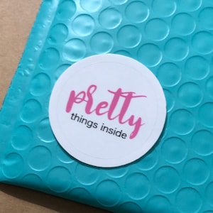 May include: A turquoise blue padded envelope with a white circle sticker that says "pretty things inside" in pink cursive lettering.