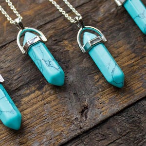 May include: Four turquoise crystal point pendants on silver chains. The pendants are hanging on a wooden surface.