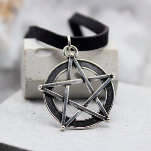 May include: A silver pentagram pendant with a black suede choker necklace. The pendant is a five-pointed star with a circle around it.