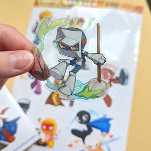 May include: A clear sticker featuring a cartoon robot character with a silver helmet, blue and orange clothing, and a green slime effect. The robot is holding a wooden stick and standing on a green rock.