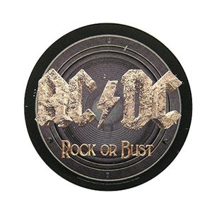 May include: A round black and silver sticker with the AC/DC logo in gold lettering and a lightning bolt. The text "Rock or Bust" is written in gold below the logo.