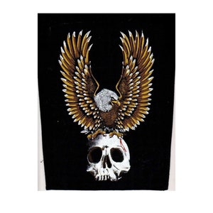 Könnte beinhalten: Ein schwarzer Patch mit einem goldenen Adler, der auf einem weißen Schädel sitzt. Der Adler hat seine Flügel weit ausgebreitet und blickt nach vorne. Der Schädel hat eine rote Markierung an der Seite.