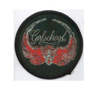 May include: A black and red embroidered patch with the text "Girlschool" in silver lettering. The patch features a pair of red wings with a silver skull in the centre.