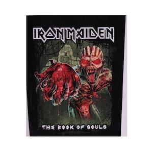 Könnte beinhalten: Iron Maiden Band-Patch mit einer roten und schwarzen Illustration einer Kreatur, die ein Herz hält. Der Text "The Book of Souls" befindet sich unter dem Bild.