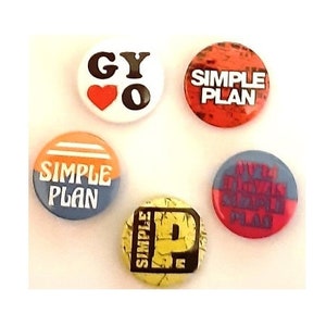 Puede incluir: Cinco botones redondos con diferentes diseños. Los botones son todos blancos con texto negro y acentos rojos, naranjas, azules y amarillos. El texto en los botones incluye "Simple Plan", "GYO" y "My First  Breakup  Album".