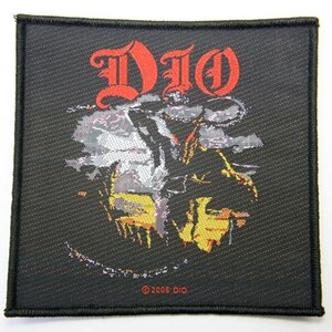 May include: Black woven patch with the word "DIO" in red stylized lettering. The patch features a black and white image of a person with a yellow and orange background. The text "© 2005 DIO" is in the bottom center of the patch.