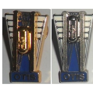 May include: Two gold and silver Otis elevator pins. The pins are in the shape of an elevator with the Otis logo at the bottom.