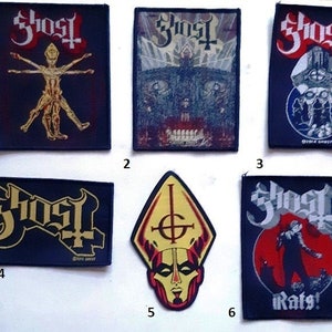 May include: A selection of six embroidered Ghost band patches. The designs include the band's logo, a Vitruvian Man-style figure, a skull-faced character, and the word "Rats!". The patches are mainly black, red, white, and gold in colour.