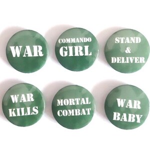 May include: Six green camouflage button pins with white text. The pins read "WAR", "COMMANDOGIRL", "STAND & DELIVER", "WAR KILLS", "MORTAL COMBAT", and "WAR BABY".