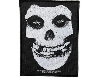 May include: Black and white iron-on patch featuring a grinning skull with a white background. The patch has the text "TM & © 2002 CYCLOPIAN MUSIC INC. WWW.MISFITS.COM" at the bottom.