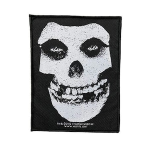 May include: Black and white iron-on patch featuring a grinning skull with a white background. The patch has the text "TM & © 2002 CYCLOPIAN MUSIC INC. WWW.MISFITS.COM" at the bottom.