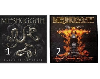 May include: Two black embroidered patches with the band name "Meshuggah" in gold lettering. The first patch features a silver snake design and the text "Catch Thirtythree". The second patch features a fiery orange and yellow design with the text "Nothing".