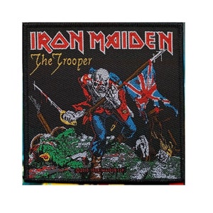 May include: Iron Maiden The Trooper band patch. A black patch with a red, white, and blue Union Jack flag, a red and black sword, and a soldier in a red and blue uniform. The text "Iron Maiden" and "The Trooper" are in white.