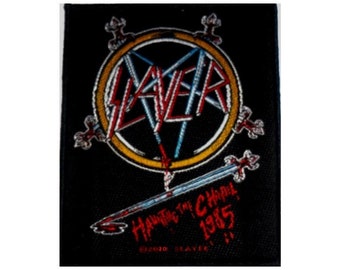 May include: Black and white embroidered patch with a red and blue Slayer logo in a yellow circle. The text "Haunting the Chapel 1985" is embroidered in red below the logo.