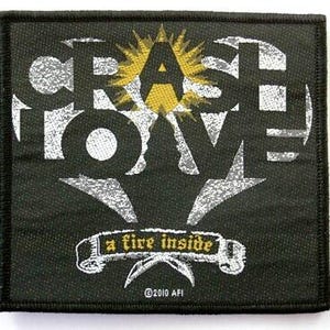 May include: Square black patch with white and gray text that reads "CRASH LOVE" with a yellow sunburst behind the letter "A". Below the text is a banner that reads "a fire inside". The patch has a black border.