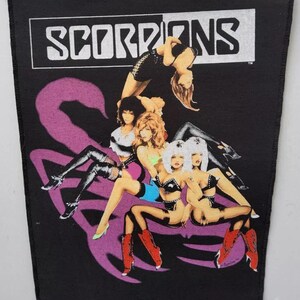 May include: Black patch with the band name "SCORPIONS" in white above a graphic of women in various poses. A large purple scorpion tail design is also present.