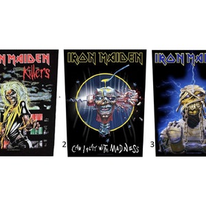 May include: Three Iron Maiden band back patches. The first patch is black with a yellow, red, and white image of Eddie, the band's mascot, with the text "Iron Maiden Killers". The second patch is black with a blue and yellow image of Eddie's head with the text "Can I Play With Madness". The third patch is black with a blue and yellow image of Eddie with the text "Iron Maiden".