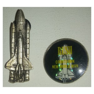 May include: A silver space shuttle pin with a black and silver pin featuring the band Rush and the text "Countdown New World Man".