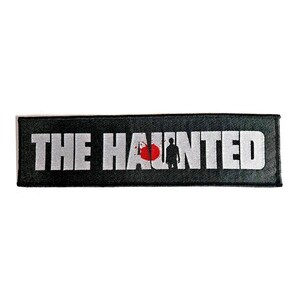 May include: A rectangular black patch with the words "THE HAUNTED" in large, white, block letters. A red target with a silhouette of a person is between the words. The patch is likely for a jacket or bag.