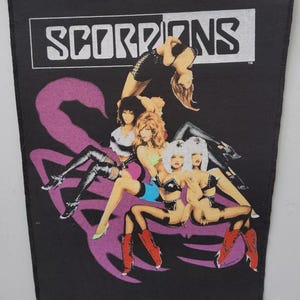 May include: Black patch with the band name "SCORPIONS" in white. The image shows several women in various poses, with a large purple scorpion graphic behind them. The women are wearing black and colorful outfits.
