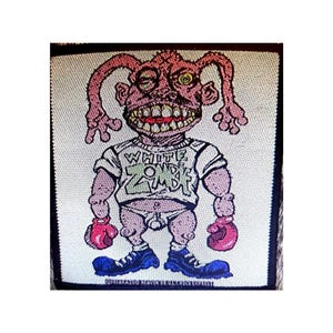May include: White Zombie band patch with a cartoon character wearing a white shirt with the band's name on it. The character is pink with green eyes and is wearing boxing gloves.