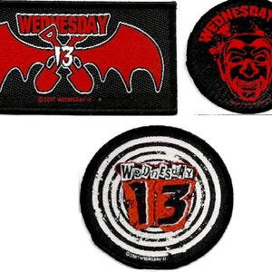 May include: Three black and red embroidered patches with the band name "Wednesday 13" in white lettering. The first patch features a red bat with crossed axes. The second patch features a red and black illustration of a clown's face. The third patch features a red and black target with the number "13" in the center.
