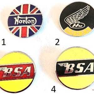 May include: Four vintage motorcycle badges. The first features the Norton logo over a Union Jack design. The second has a Honda wing logo. The third and fourth have BSA logos with wing designs. All are circular with metallic borders.
