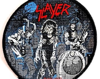 May include: A black and white embroidered patch with the word "Slayer" in red lettering. The patch features a skeletal figure with a guitar and a dark background.