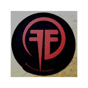 May include: A black and red embroidered patch with the letters "FF" in a circle. The patch is made of fabric and has a stitched edge.