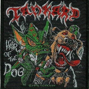 May include: A black embroidered patch with the band name "Troglodyte" in red and white lettering. The patch features a green and orange monster with a cigarette and a red and orange dog with sharp teeth. The text "War of the Dog" is written in white on the left side of the patch.