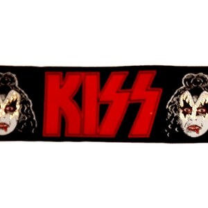 May include: Black fabric patch with the word "KISS" in red letters and two black and white images of faces with makeup on either side.