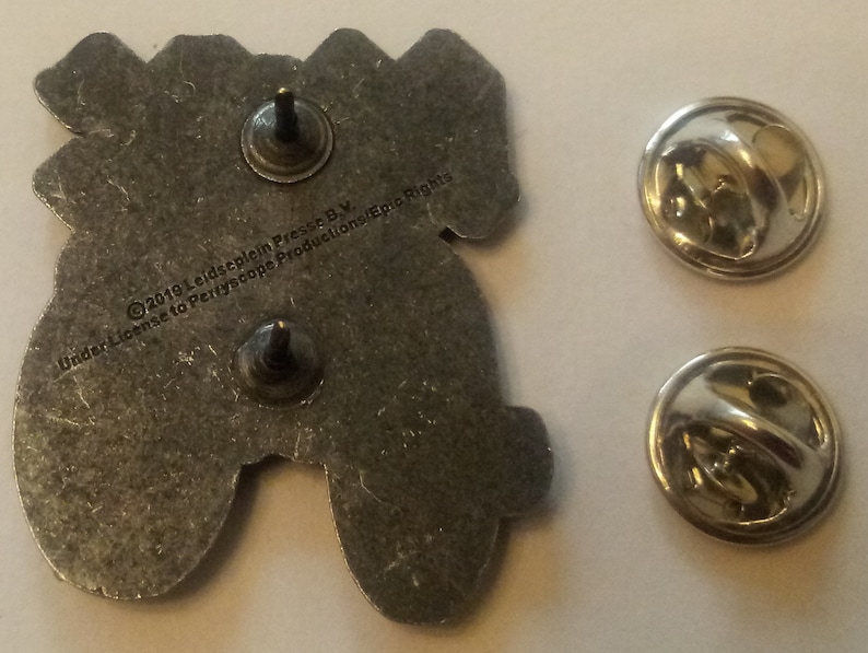 May include: A silver metal pin featuring a cartoon image of a video game controller. The back of the pin has the text "&copy;2019 Leidscheplein Press B.V. Under License to Periscope Productions/Epic Rights".