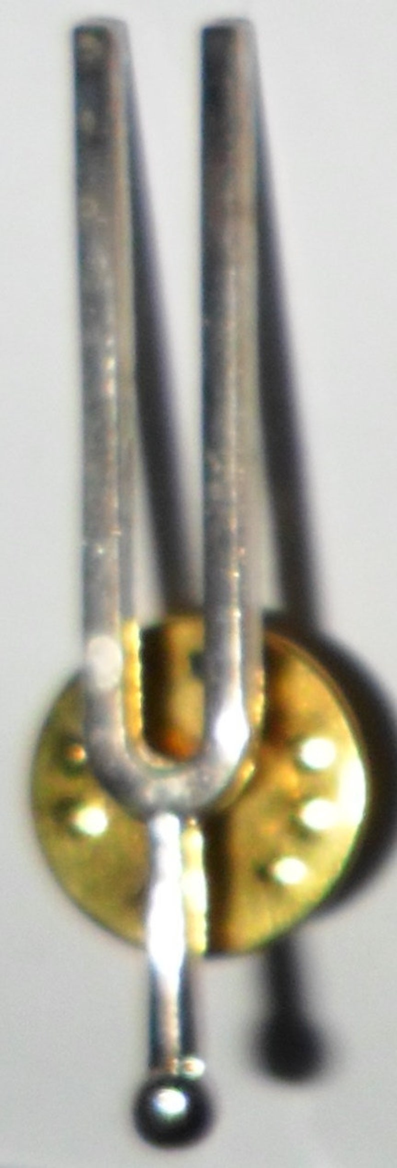 Puede incluir: Un diapas&oacute;n de plata con una base redonda dorada. El diapas&oacute;n se utiliza para crear un tono espec&iacute;fico para instrumentos musicales.