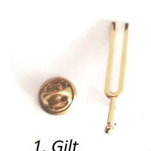 Puede incluir: Un diapas&oacute;n dorado y un alfiler dorado con cabeza redonda. El texto "1. Gilt" es visible debajo del alfiler.