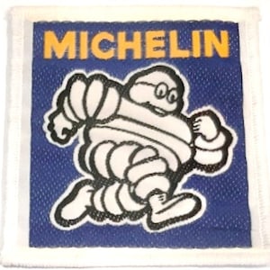 May include: A white patch with a blue background featuring the Michelin Man, a white cartoon figure wearing glasses and running, with the word "MICHELIN" in yellow letters at the top.