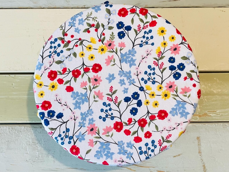 Reusable bowl covers in "Wildflower" print: a vibrant floral pattern on a white background. The design features red, blue, yellow, and pink flowers with green stems and leaves. The flowers are scattered across the surface, creating a cheerful and colorful look.